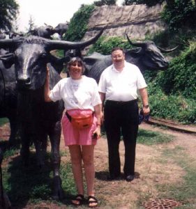 Sue Mayoff and Art Mayoff help drive cattle at Dallas City Hall, standing next to large bronze cattle