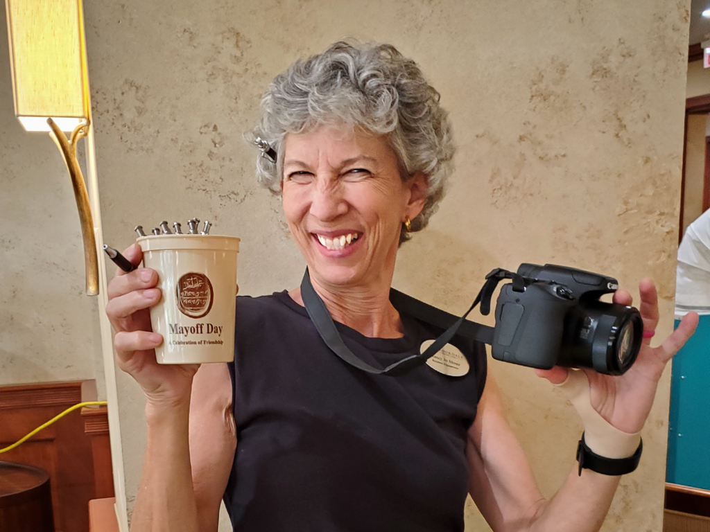 Smiling woman holding a Mayoff Day cup and a camera
