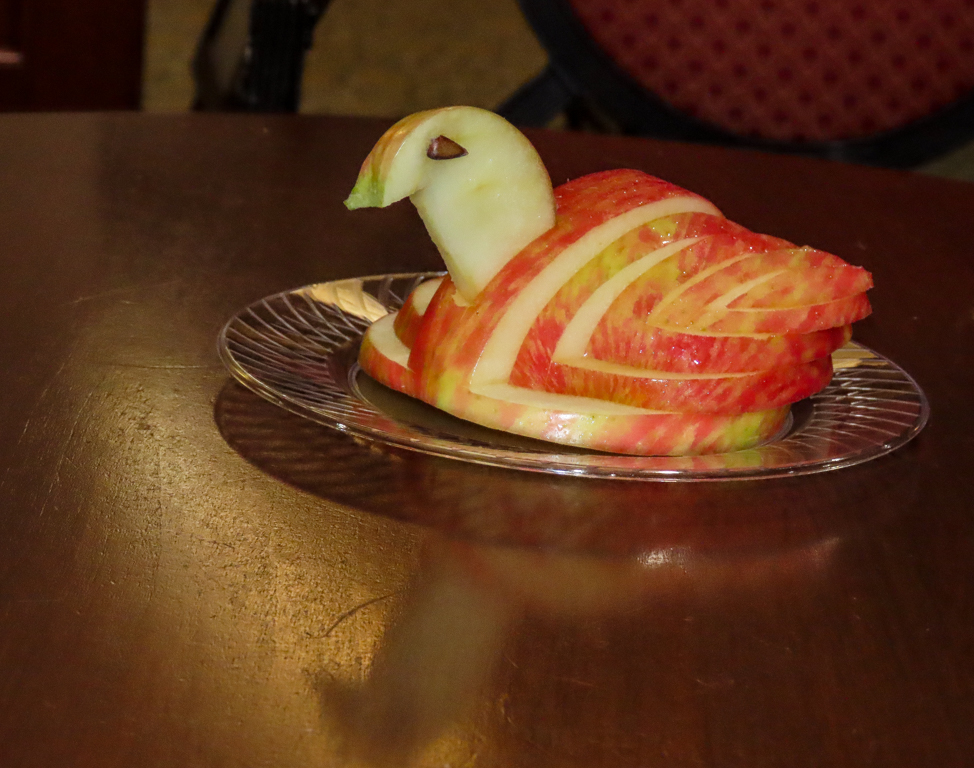 An apple carved into the shape of a swan atop a small, wooden cocktail table