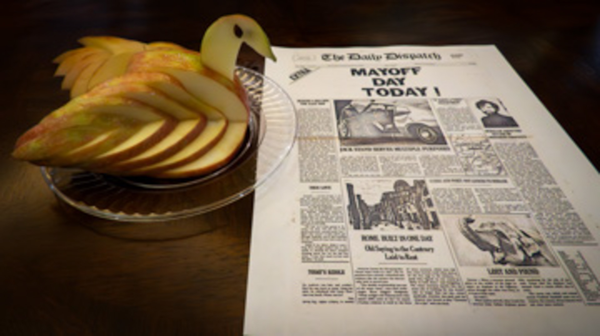 Apple carved to look like a swan next to a copy of a fake newspaper front page with the headline: "Mayoff Day Today!"