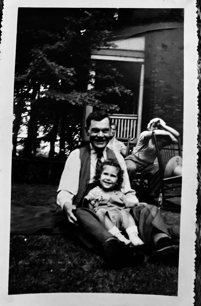 Man with vest and tie sitting on grass with a young girl on his lap