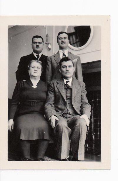 Black and white photo of older couple seated with their adult sons standing behind them, all with serious expressions