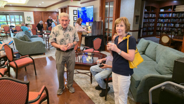 Smiling man and woman standing, facing camera, holding peach bellini glasses