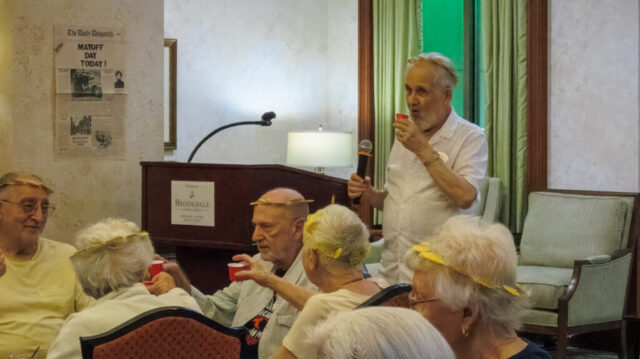 Standing man with microphone and several seated people holding glasses for a toast