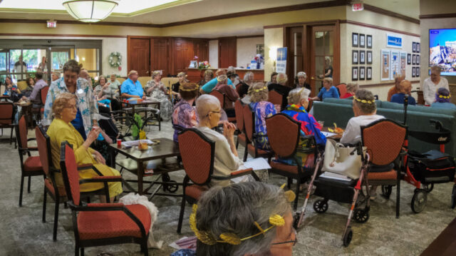 Large group of seated people wearing gold laurel leaf tiaras, some with red shot cups of ouzo