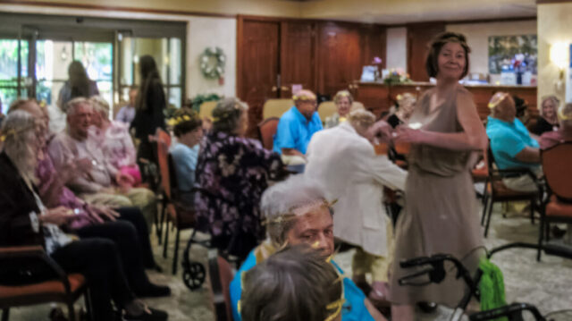 Activity Director Terri moving rapidly amongst seated crowd while passing out frozen bellinis