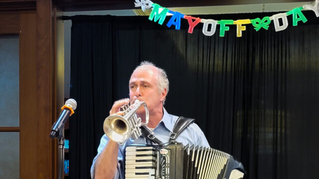 Oli blows his cornet for Mayoff Day Man blowing cornet under Mayoff Day banner