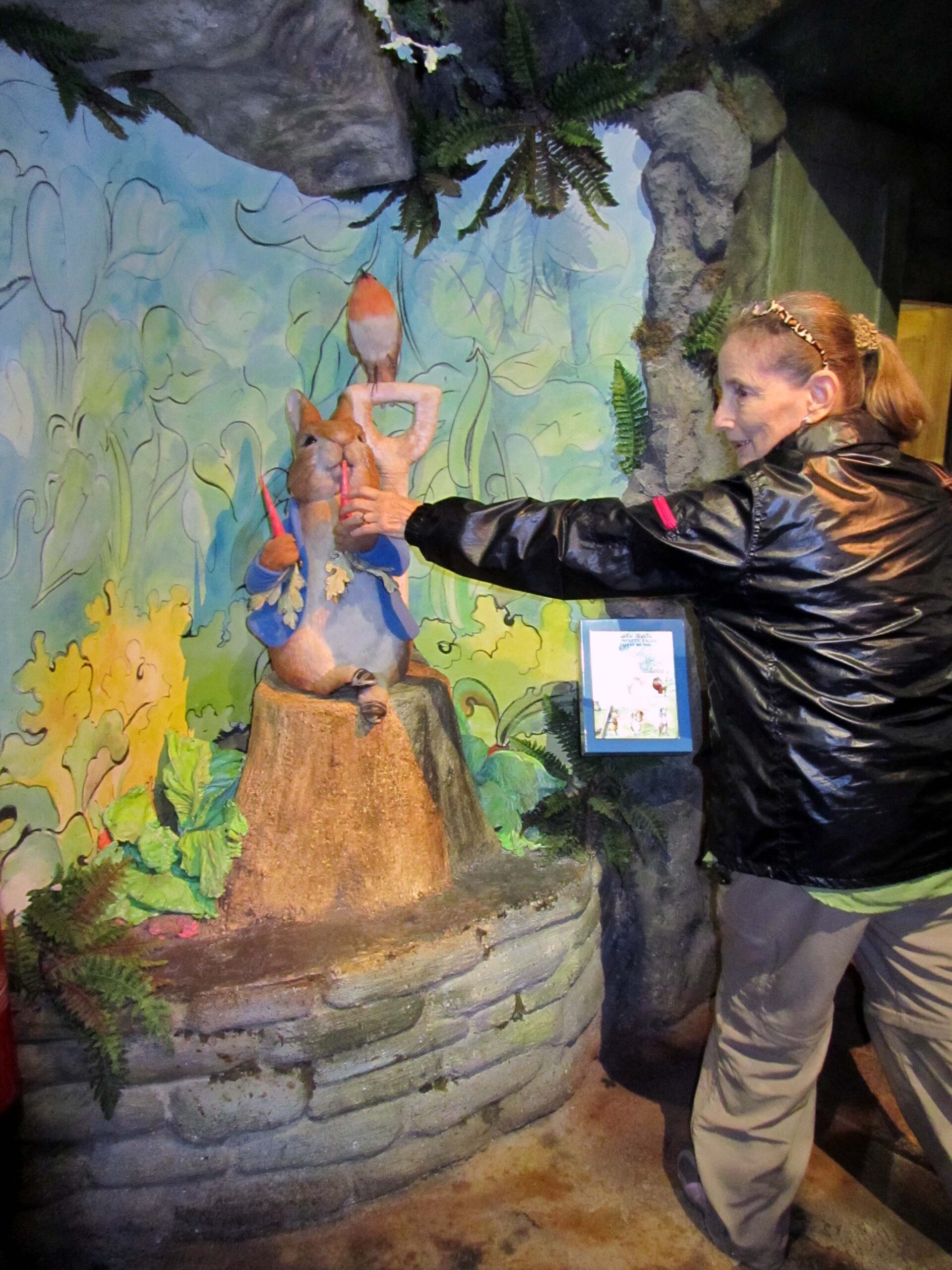 Denise reaching for one of the carrots held by a life-size Peter Rabbit statue at the Peter Rabbit exhibition in Bowness-on-Windermere